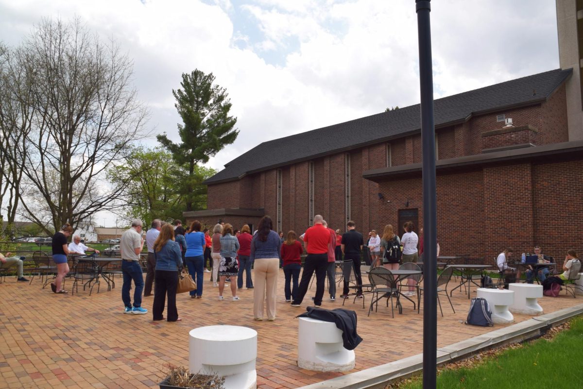 Dozens of faculty and students gather around Rev. Mara Bailey as she shares a few words prior to the moment of silence